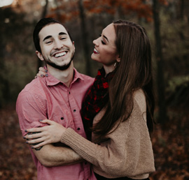 A photo of a couple hugging each other with autumn trees in the background